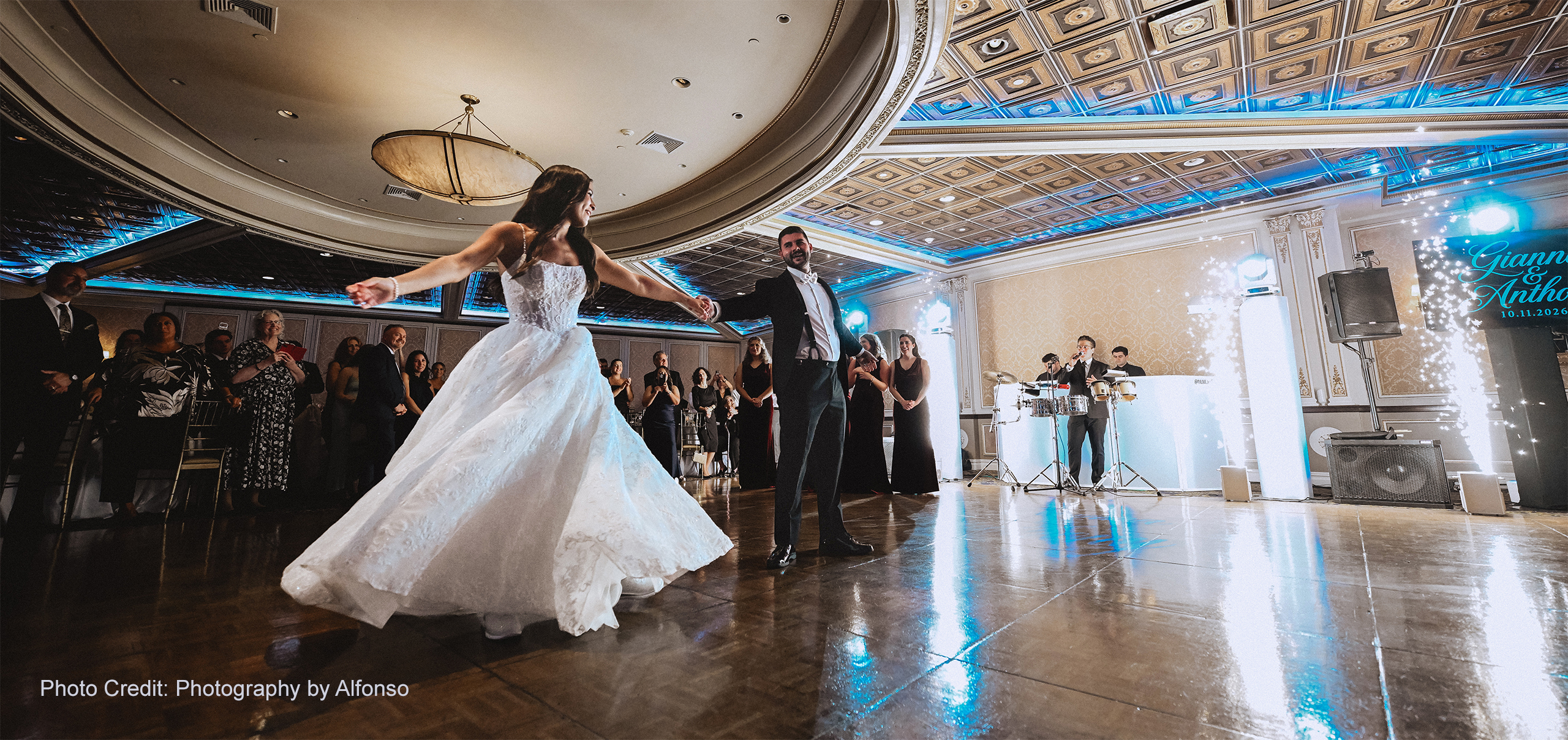 Bride and groom celebrating their wedding reception on the dance floor with DJ Live entertainment, blue uplighting, and indoor sparkler effects. Photo by Photography by Alfonso